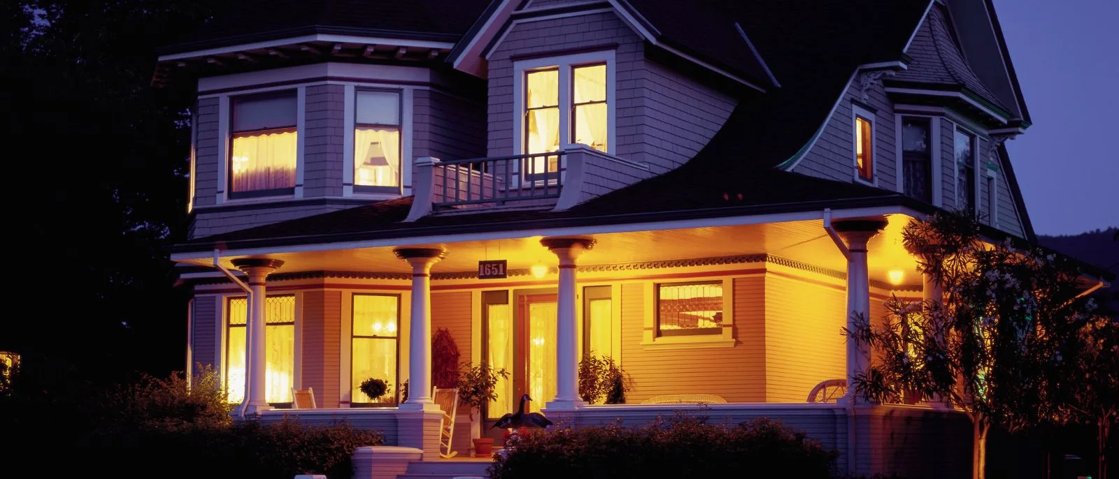A lit house with a wraparound porch at dusk